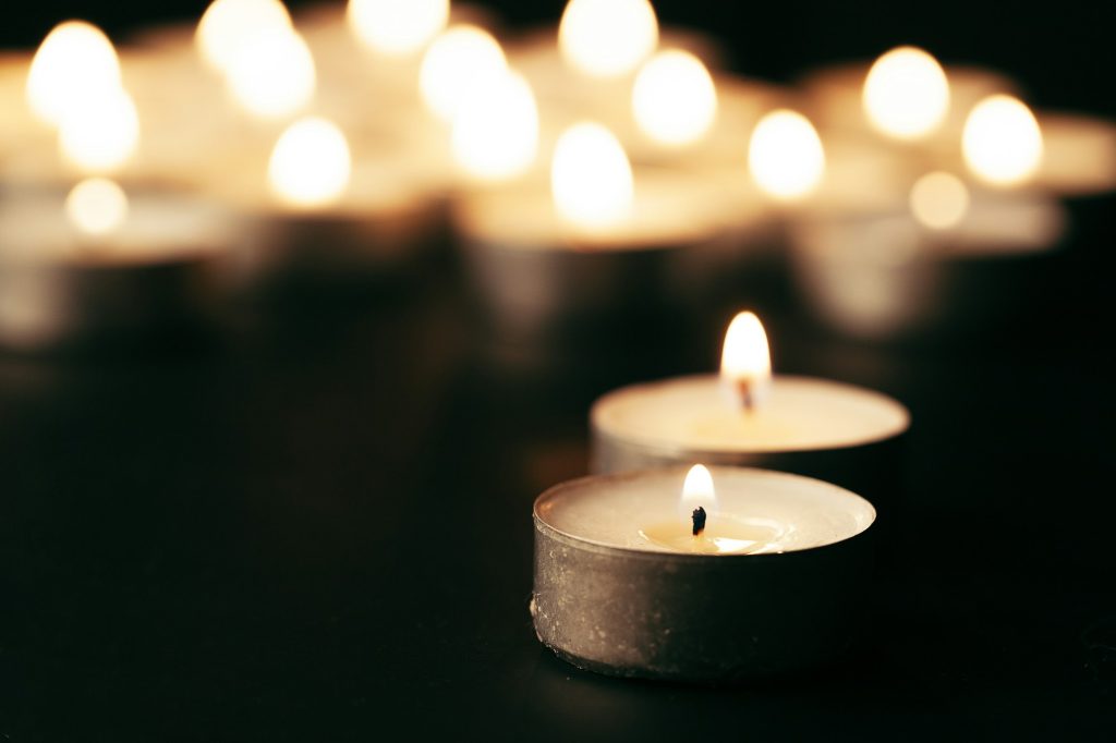 Burning candle on table in darkness, space for text. Funeral symbol
